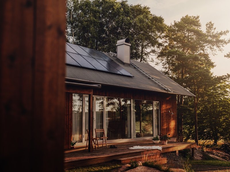 Holzhaus in der Natur mit Photovoltaik auf dem Dach. (Was kostet die Zulassung einer Solaranlage?)